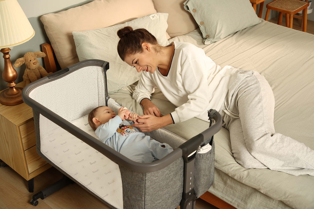 A mom lays next to a baby in a bassinet 