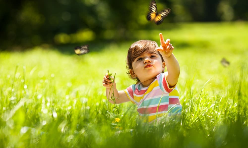 A toddler sits outside in a field enjoying spring activities for preschoolers 