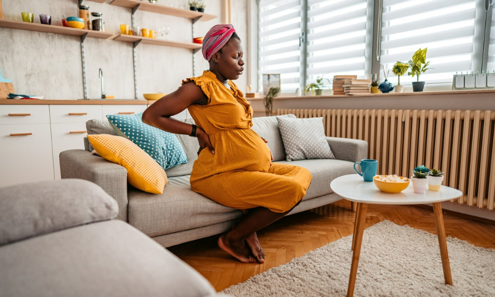 A pregnant woman on a couch feeling pregnancy symptoms 